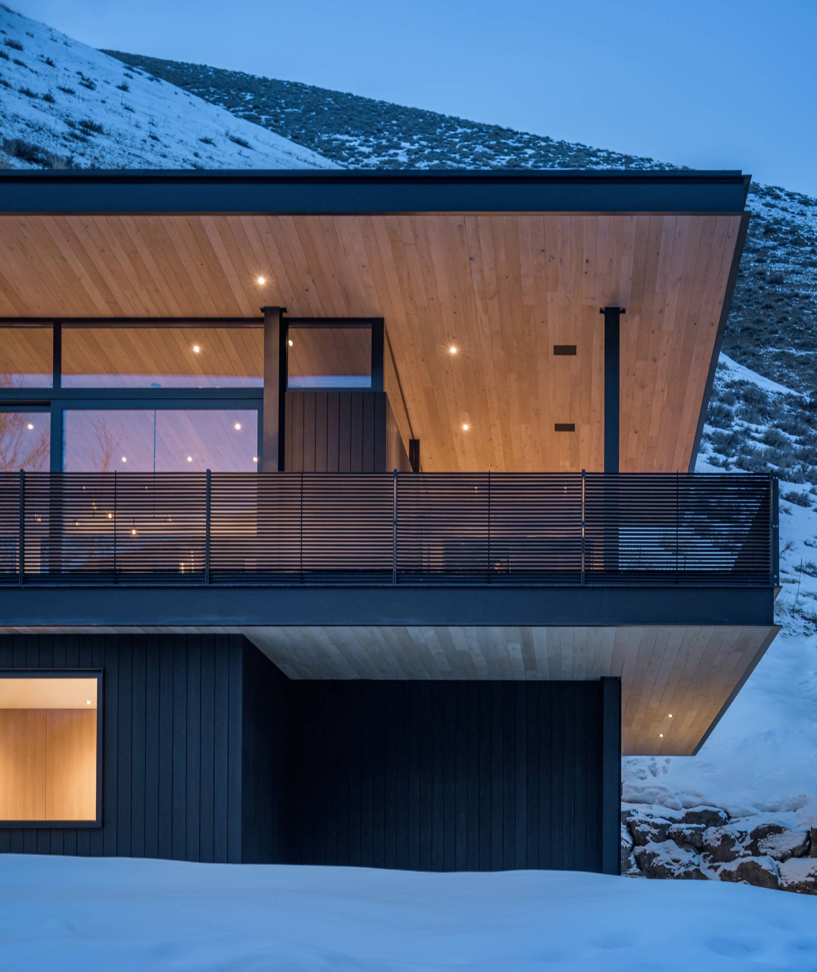 Exterior view of the upper deck at night at Avalanche Chalet, a custom home designed and built by Farmer Payne Architects.