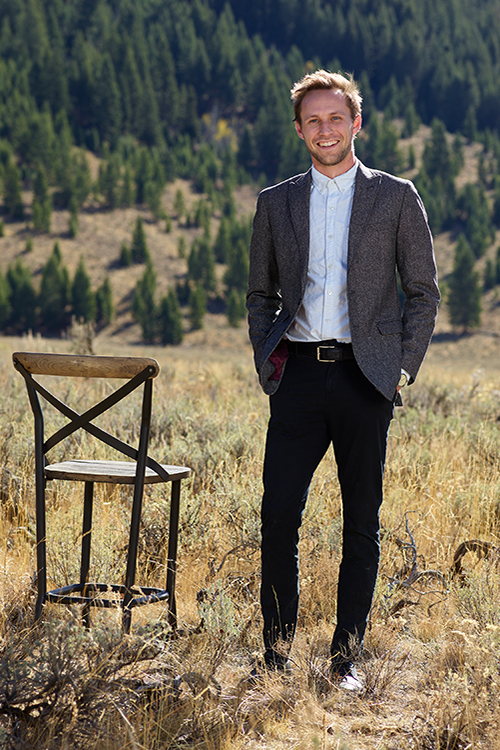 Farmer Payne Architects Associate Aaron Belzer stands next to a chair in a field in Jackson Hole.