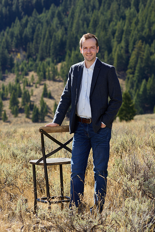 Farmer Payne Architects Project Manager Casey Fair stands next to a chair in a field in Jackson Hole.