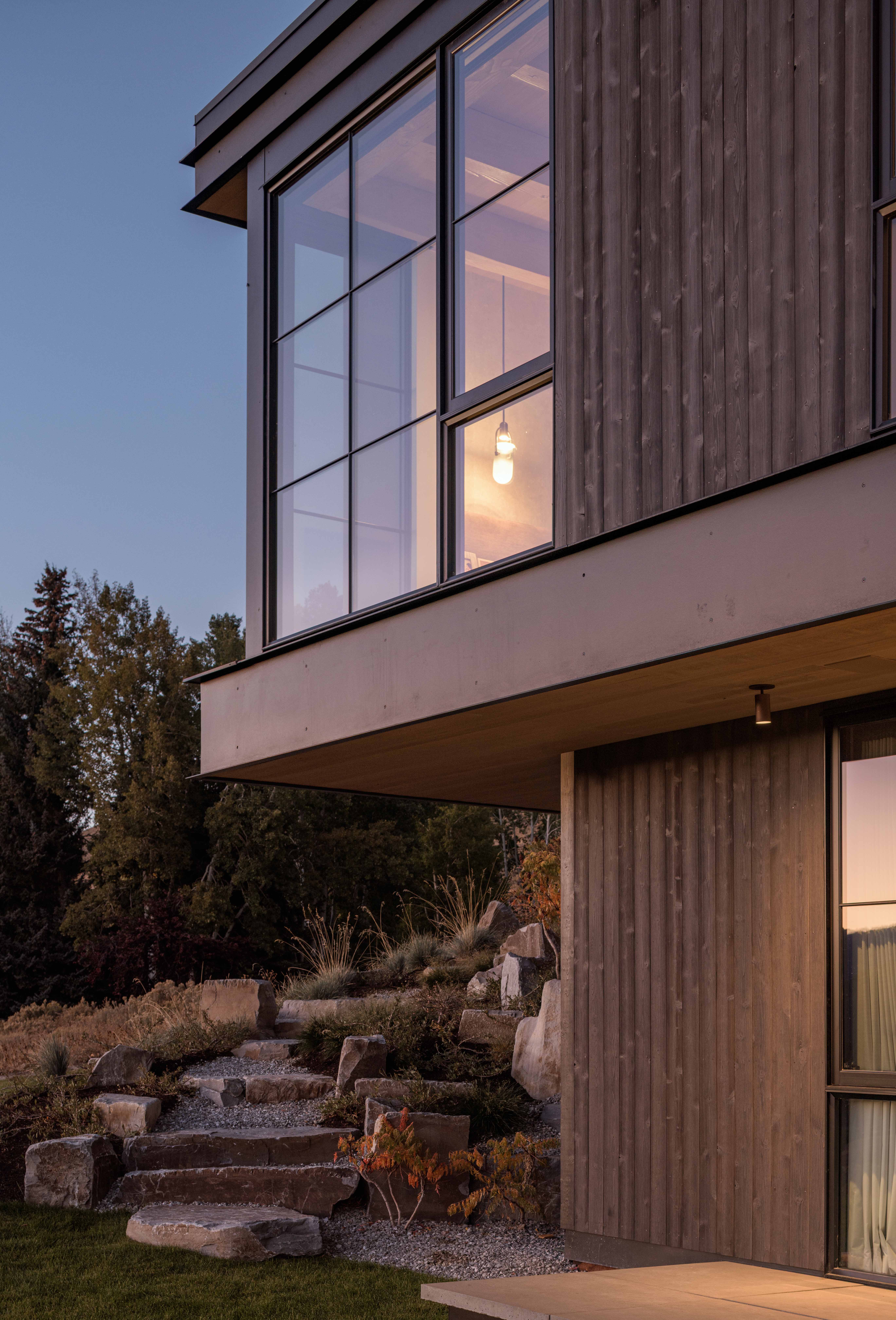 contemporary mountain home exterior, featuring dark hewn siding, master bedroom cantilevered edge, and landscaped rock pathway